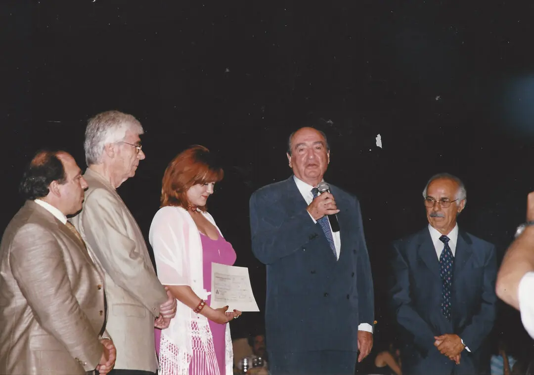 Four people standing on a stage, one speaking into a microphone.