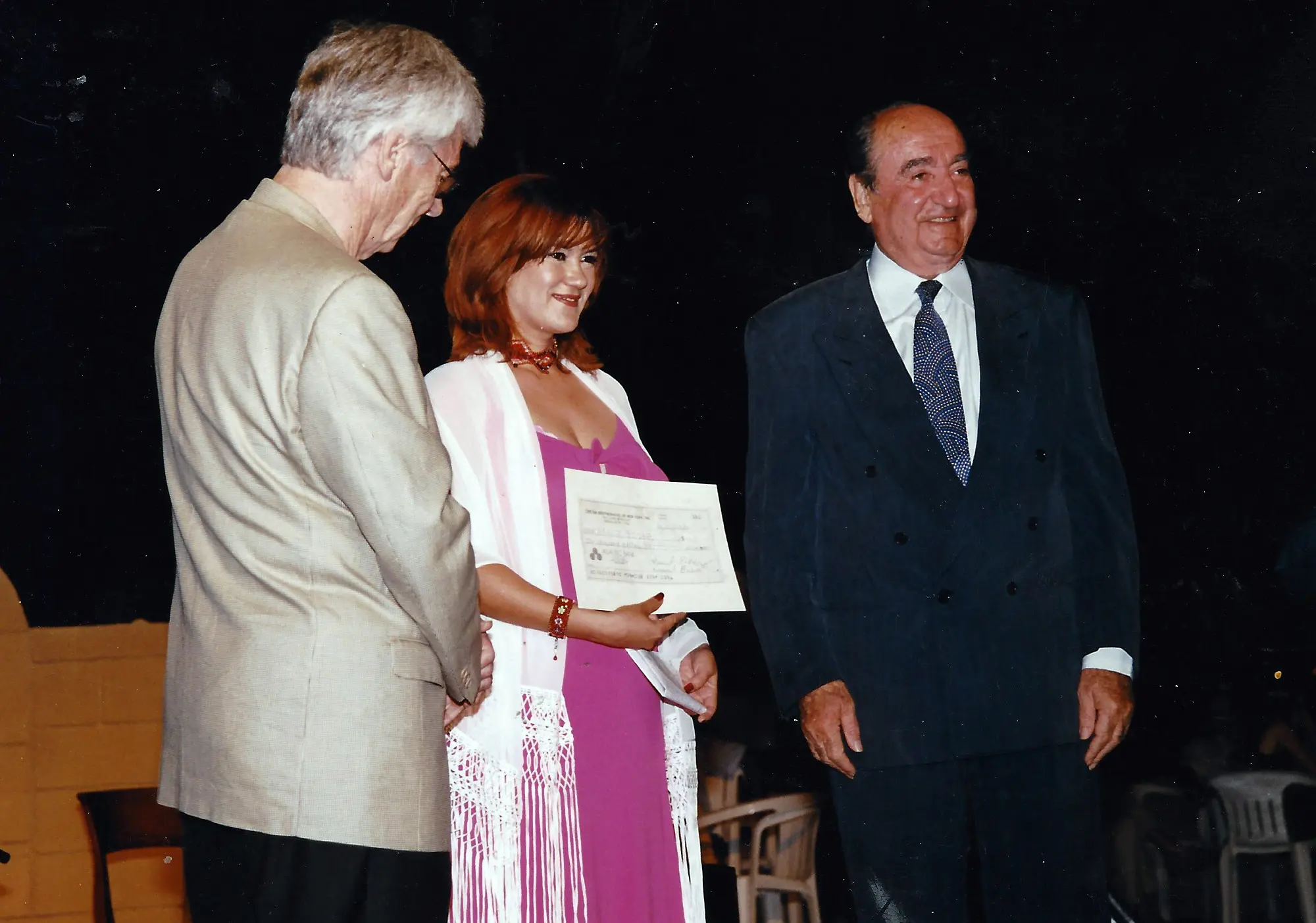 Three people on stage during a certificate presentation ceremony.