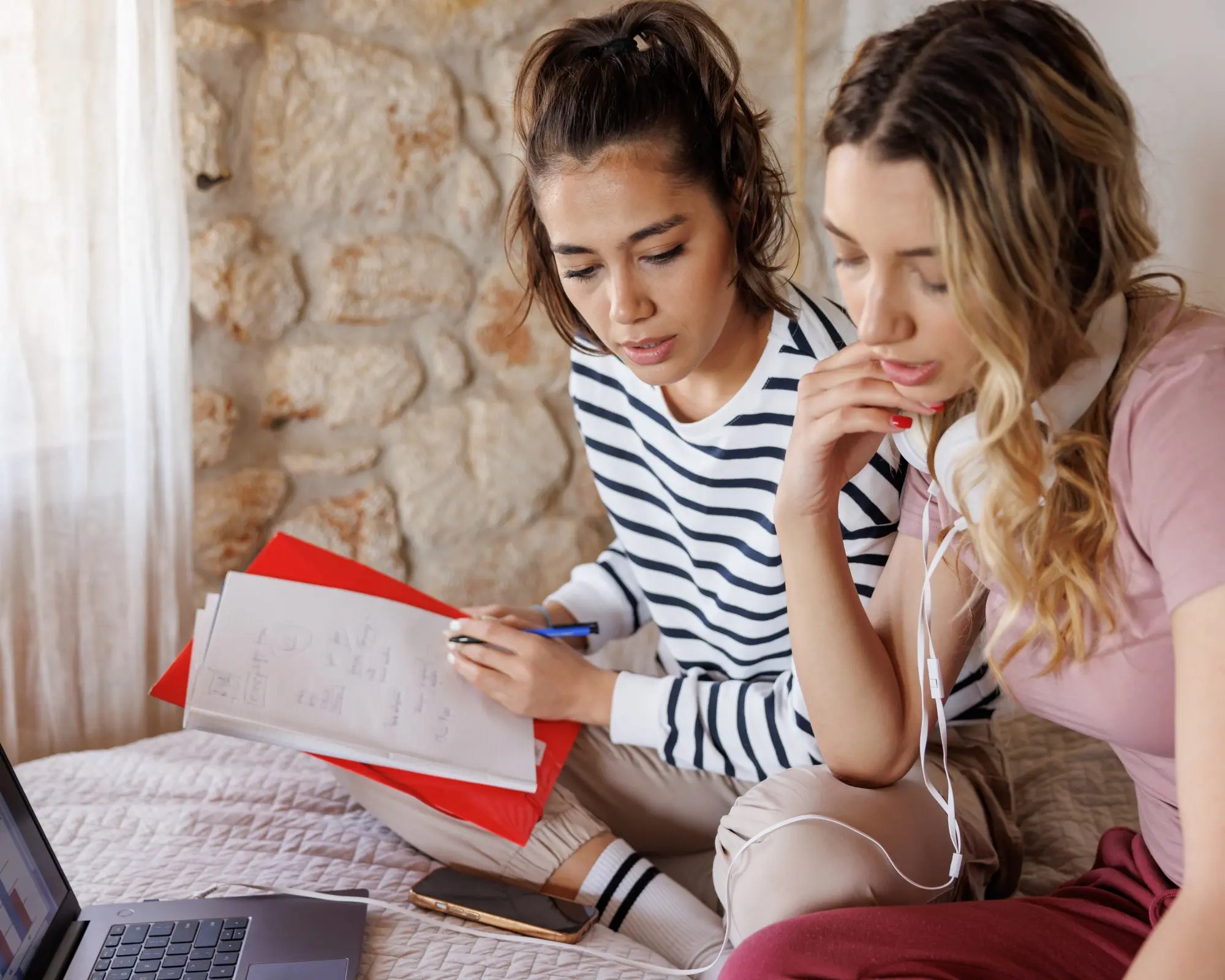 Two women studying with laptop and papers.