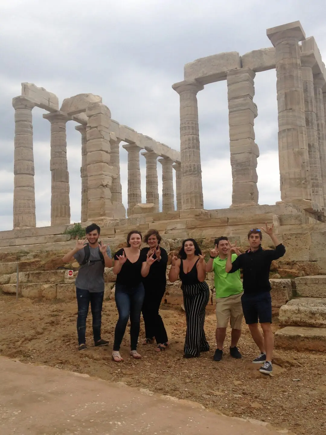 Group posing joyfully in front of ancient Greek ruins.