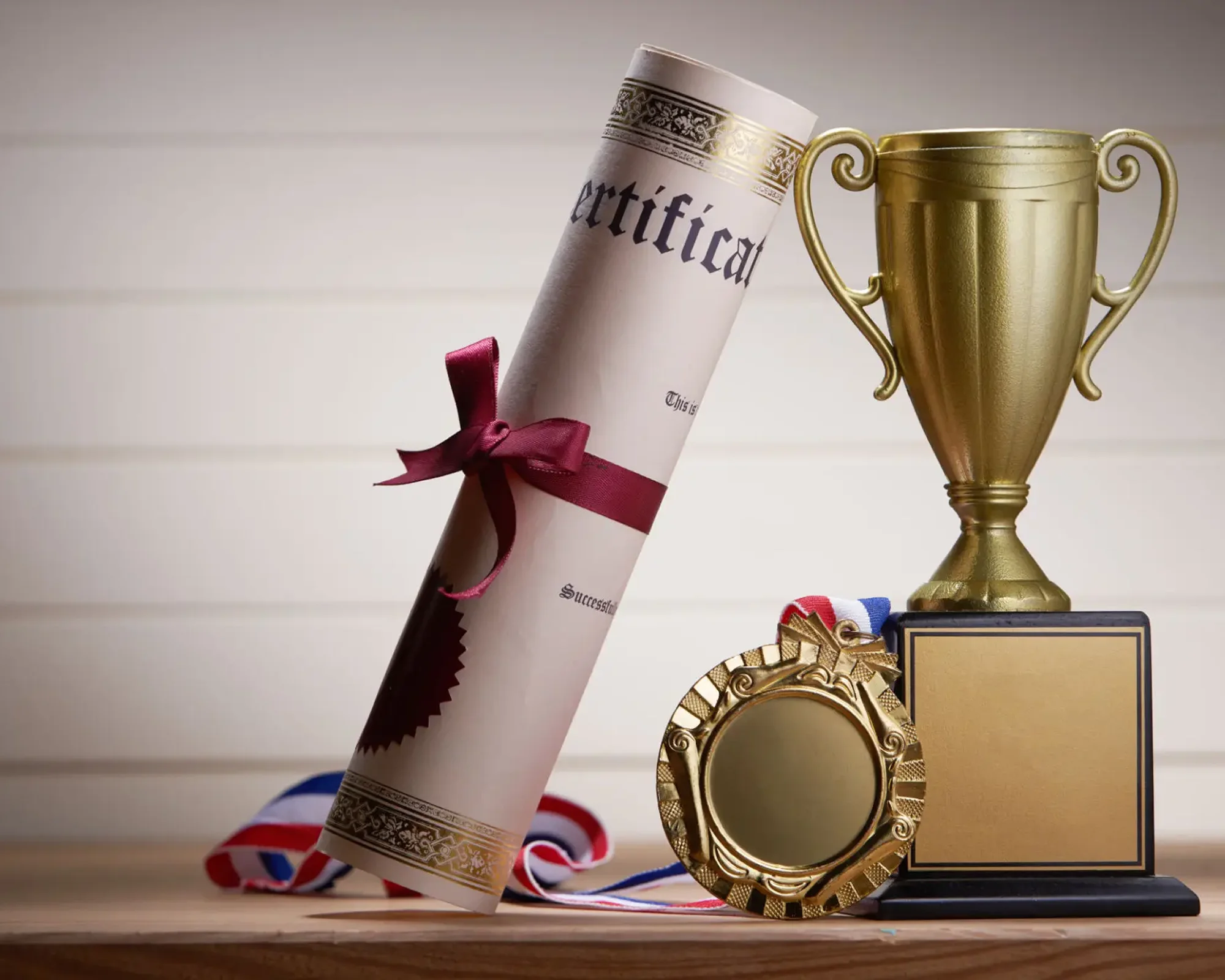 A rolled-up certificate, medals, and a trophy on display.